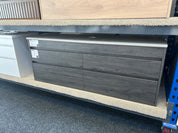 A dark gray wood-grain four-drawer dresser or storage cabinet with a light gray top surface, shown on a store display shelf.