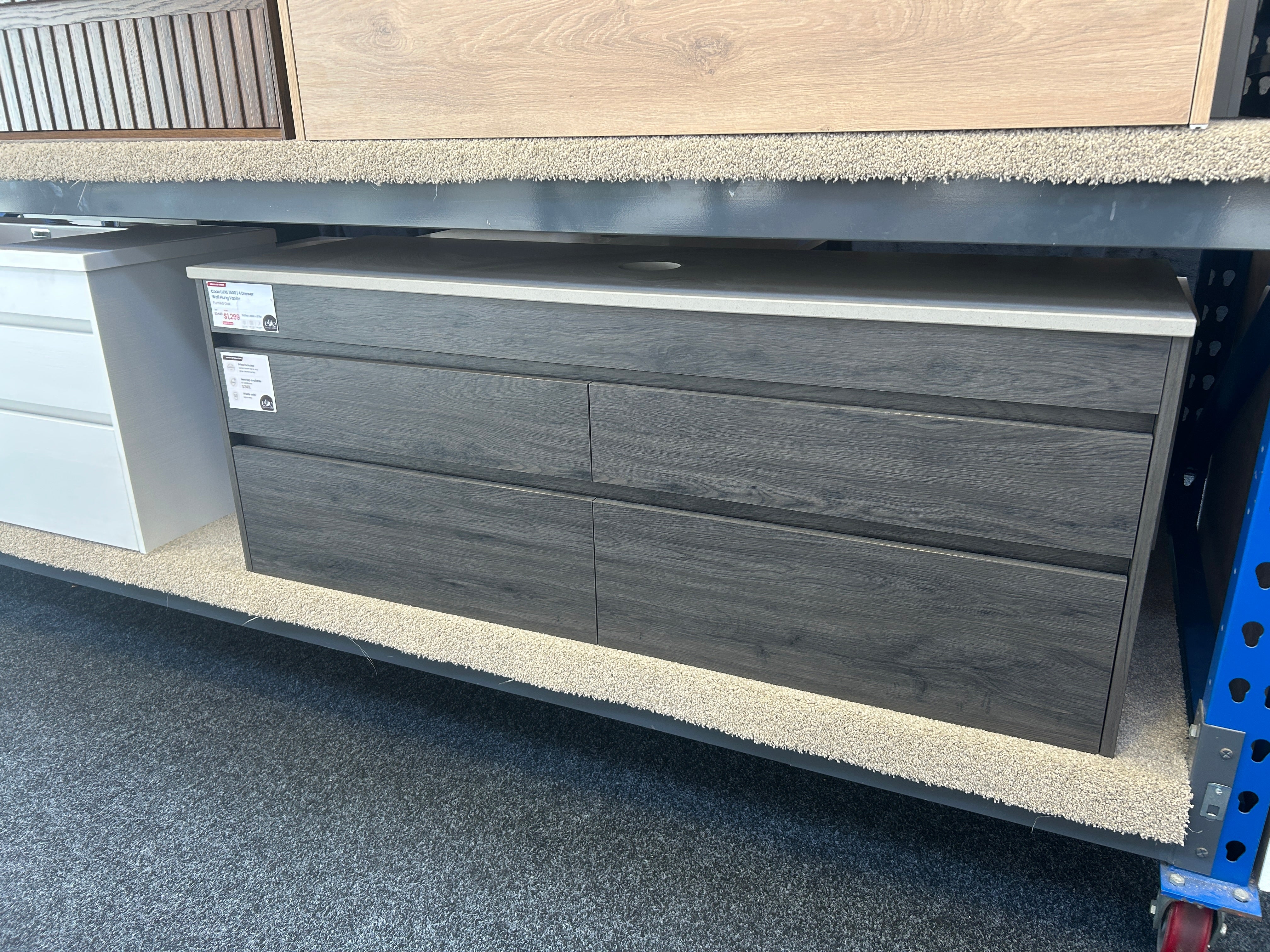 A dark gray wood-grain four-drawer dresser or storage cabinet with a light gray top surface, shown on a store display shelf.