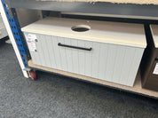 A light gray cabinet with a cream countertop and a black pull handle, photographed on a store shelf with carpeted floor and shelving visible.