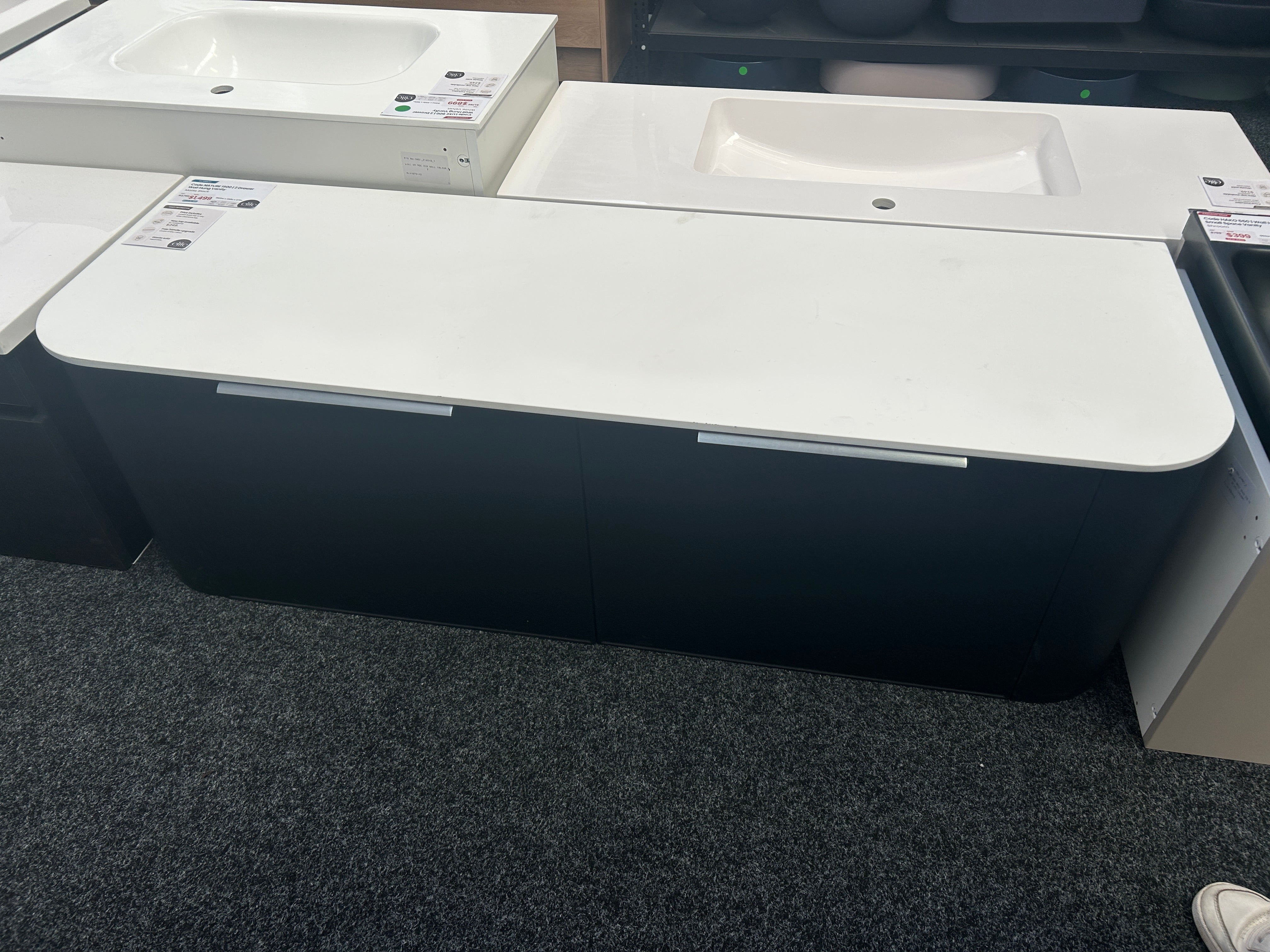 A modern bathroom vanity cabinet with a white countertop and integrated sink, shown in a showroom setting with other similar units in the background.